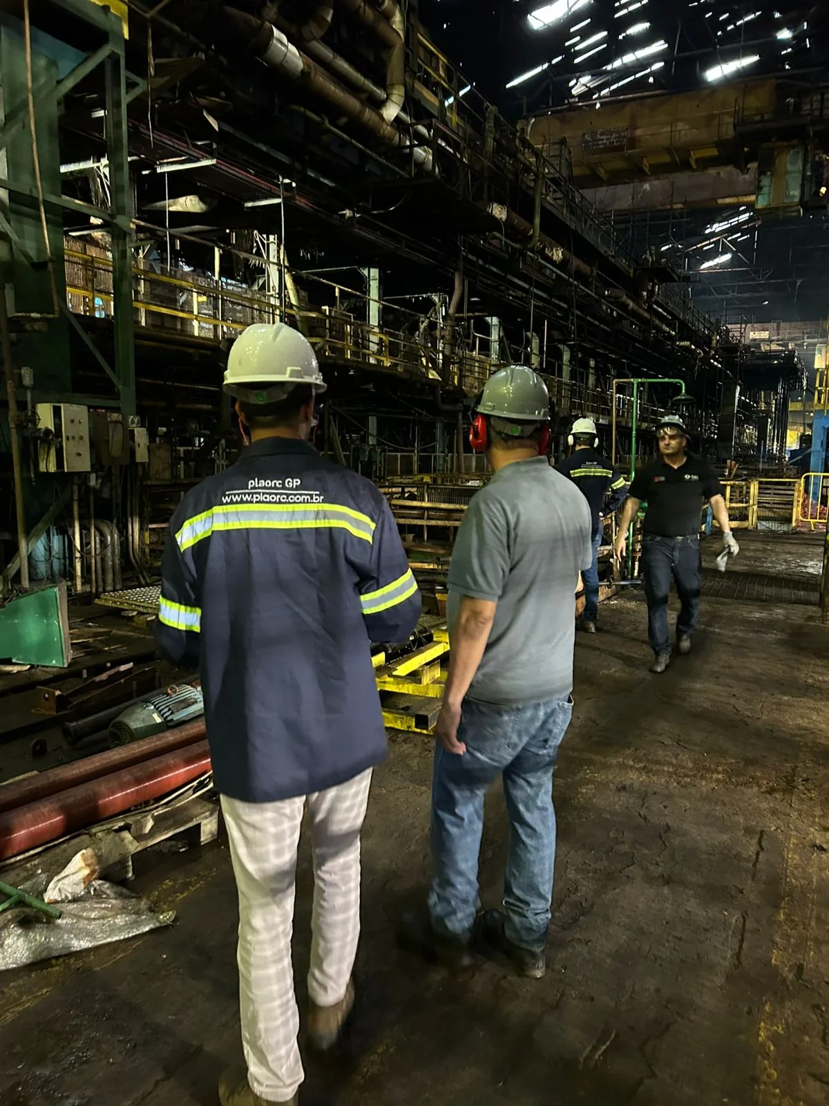 Profissionais da PLAORC discutindo o planejamento em campo, dentro de estrutura metálica de planta industrial